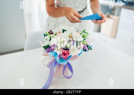 Giornata delle donne. La ragazza apre la busta con la carta lasciata nel mazzo di fiori in scatola regalo sulla cucina. Sorpresa presente Foto Stock