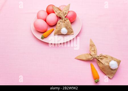 Concetto di uova di Pasqua, decorazione della disposizione del tavolo. Uova rosa (rosate) con bunny (coniglio) carta regalo uovo di imballaggio su piastra con carote lavorato a maglia. Panno ( Foto Stock