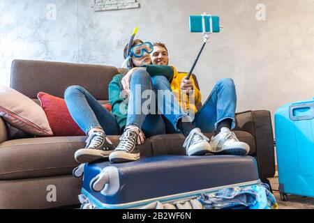 giovane coppia seduto sul divano a casa prende un selfie con smartphone che indossa una maschera subacquea prima di partire per la vacanza Foto Stock