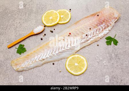 Filetto di nasello fresco crudo su fondo di pietra. Con limone, prezzemolo, sale in cucchiaio di legno e peperoni mescolare. Foto Stock