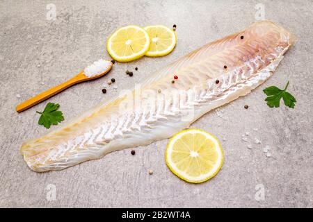 Filetto di nasello fresco crudo su fondo di pietra. Con limone, prezzemolo, sale in cucchiaio di legno e peperoni mescolare. Foto Stock