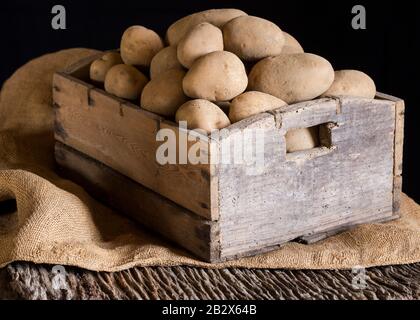 Patate fresche in una vecchia scatola di legno su un sacco e una tavola di legno Foto Stock