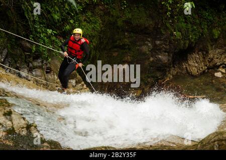 Donna adulta indossare equipaggiamento impermeabile scendendo una cascata Foto Stock