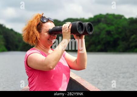 Visitor Female With High Power Binocolo In Amazonian Forestry Contro La Fitta Vegetazione Foto Stock