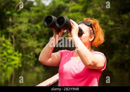 Tourist Woman Con High Power Binocolo Nella Giungla Amazzonica Contro La Fitta Vegetazione Foto Stock