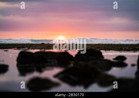 (Fuoco selettivo) splendida vista delle onde che si infrangono durante un tramonto drammatico e romantico sullo sfondo. Lombok Island, Indonesia. Foto Stock