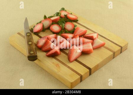 Pulizia e affettatura di fragole rosse fresche crude su tagliere di legno con coltello Foto Stock