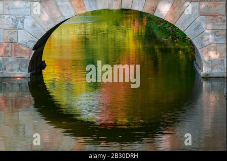 Impressioni Autunnali. Foglie colorate riflesse in un ruscello, vista attraverso l'arco di un ponte. Foto Stock