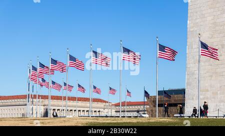 Bandiere americane che sventolano alla base del monumento di Washington di giorno libero e soleggiato in D.C. Foto Stock