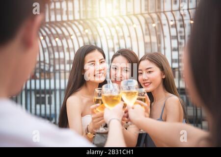 Un gruppo di persone asiatiche di sesso multiplo che tiene un bicchiere di vino chiacchierano con gli amici mentre celebrano una festa di danza sul nightclub all'aperto sul tetto. Foto Stock