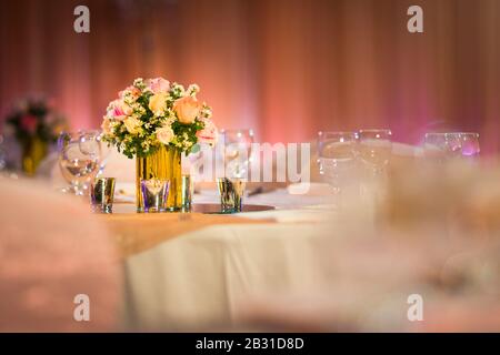 Fiorista di rose in vaso di vetro decorazione sul tavolo da cena con argenteria e candela indiano nozze impostazione al coperto con luci decorative e bella boke Foto Stock