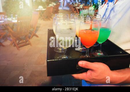 Cameriera portare vassoio di bicchieri da drink di benvenuto per un nuovo cliente di benvenuto in hotel di festa nuhtclub e ristorante, frizzante vita notturna sul retro Foto Stock