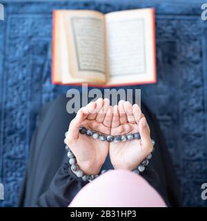 lato di giovane asiatico bella donna musulmana pregare con le perle e leggere quran sedersi su tappeto tappeto con meditazione in moschea. Foto Stock