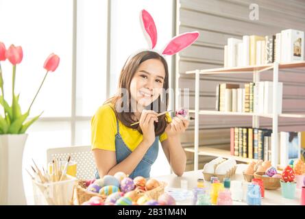 Bella giovane donna asiatica pittura uova di pasqua sul tavolo con uova decorate per celebrare aprile giorno di Pasqua con spazio copia. Foto Stock