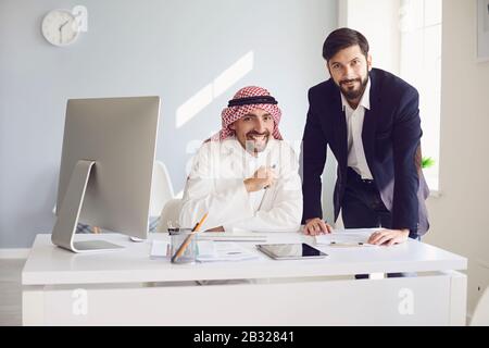 Un uomo d’affari arabo ed europeo che lavora fiducioso in un ufficio bianco. Foto Stock
