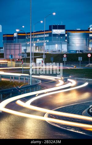 Kolbaskowo, Polonia - 28 febbraio 2020: Centro di e-commerce Amazon Robotics a Kolbaskowo con percorsi per luci auto in primo piano al tramonto. Foto Stock