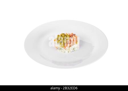 Insalata russa con piselli, pesce rosso, salmone al chum, uova, cetrioli, carote, patate sul piatto, vista laterale sfondo bianco isolato Foto Stock