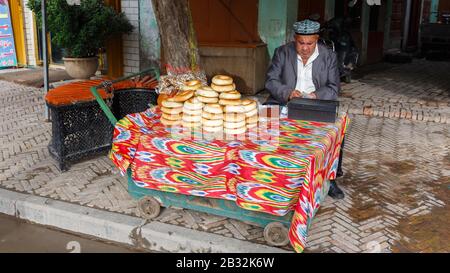 Uyghur uomo che vende Girde Naan / Nan in un mercato nelle strade di Kashgar. Il cibo tradizionale locale, che per gli occhi occidentali sembra simile ai bagel. Foto Stock