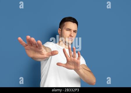 Rifiuto, disgustato. Ritratto del giovane caucasico isolato su sfondo blu studio. Bel modello maschile in stile casual, colori pastello. Concetto di emozioni umane, espressione facciale, vendite, pubblicità. Foto Stock