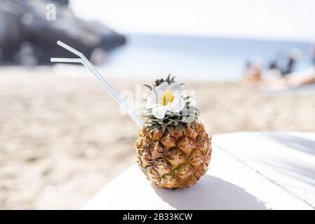 Esotico cocktail estivo a base di ananas decorato con fiori sulla spiaggia. Concetto di vacanze estive Foto Stock