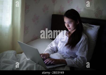 Donna asiatica che usa un notebook per lavorare la notte al bed.She sorride e ama lavorare a casa. Foto Stock