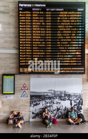 I turisti dormono e sui loro telefoni mentre aspettano all'interno della stazione ferroviaria Venezia Santa Lucia Venezia, Italia Foto Stock