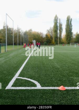 Fuoco selettivo ai coni dell'arker usati per l'addestramento di calcio sul tappeto erboso artificiale verde con i bambini blurry che addestrano lo sfondo Foto Stock