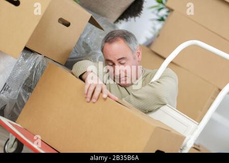 uomo di mezza età addormentato tra pile di scatole Foto Stock