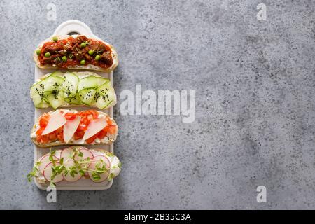 Panini con verdure, ravanelli, pomodori, cetrioli decorati con microgreens su tagliere bianco su grigio. Vista dall'alto. Spazio per il testo. Foto Stock