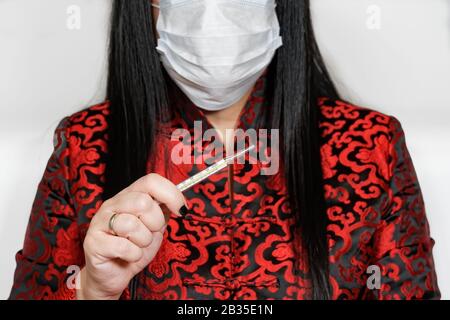 Coronavirus COVID-19 concetto con donna in vestiti asiatici indossare maschera e tenere termometro medico analogico per illustrare la protezione da malattie. Foto Stock