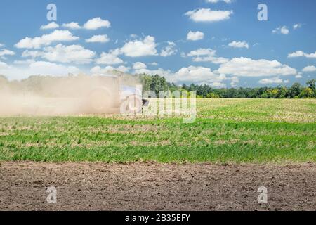 Trattore blu moderno coperto di polvere terra arando campo agricolo in fattoria in giornata di sole brillante. Coltivatore coltivando e fa terreno coltivando prima Foto Stock