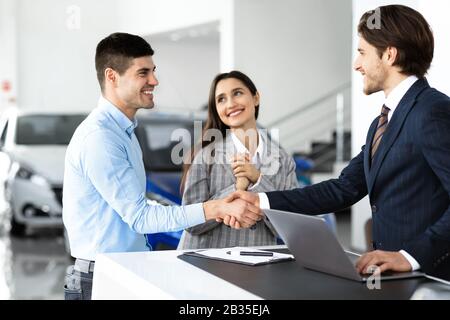 Coniugi Che Comprano L'Automobile Che Handshaking Con L'Uomo Del Venditore Foto Stock