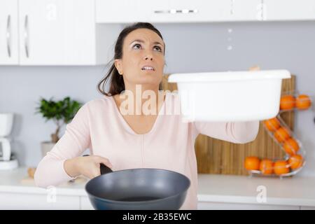 tenendo due secchi mentre gocce d'acqua perdono dal soffitto Foto Stock