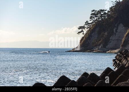 Un surfista guida un'onda verso Capo Imamuragasaki, Sagami Bay, vicino all'Isola di Enoshima, che ospita gli eventi di vela delle Olimpiadi estive di Tokyo 2020 Foto Stock