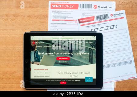 Il sito di trasferimento di denaro moneygram visualizzato su un tablet ipad insieme a moduli stampati per l'invio e la ricezione di denaro. Foto Stock