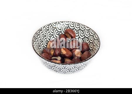 Vista dall'alto su Conkers (castagne a cavallo) in ciotola di design bianco e nero su sfondo bianco studio Foto Stock