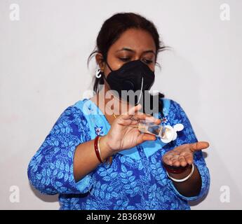 Usando l'igienizzatore o l'igienizzatore della mano e indossando la maschera protettiva della faccia una signora indiana che prende la prevenzione contro il virus della corona o l'influenza del covid 19 in India Foto Stock