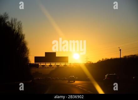 Southampton, Regno Unito - 19 gennaio 2020: La cornice Sunsilhoutetes auto e segni sulla M27 autostrada vicino a Rownhams Foto Stock