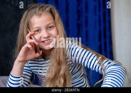 Sorridente ragazza caucasica che parla sul cellulare a casa. Guardando la fotocamera. Comunicazione a lunga distanza, chiamata, tecnologia, infanzia Moderna Foto Stock