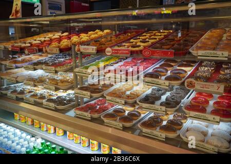 Varietà di ciambelle deliziose in vetrina presso il panificio Krispy Kreme. Vari tipi di ciambelle sul ripiano nel negozio di prodotti da forno. Selezione di dolci. Foto Stock