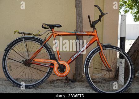 Una vecchia bicicletta arancione è in piedi sulla pista di sabbia bloccata ad un albero. Vecchio ciclo arancione Apache concatenato ad un albero. Ciclo dell'uomo con blocco nell'albero in una san Foto Stock
