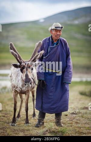 Mongolia, provincia di Khovsgol, vicino a Tsagaannuur, Taiga occidentale, campo di Tsaatan, anziano indossando abiti tradizionali e camminando per la sua renna, altitudine 2203 metri Foto Stock