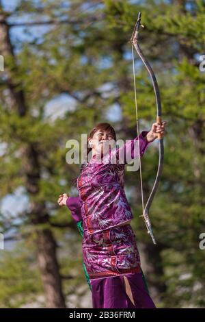 Mongolia, provincia di Khovsgol, Khatgal, festival Naadam, donna che pratica tiro con l'arco in abiti tradizionali Foto Stock