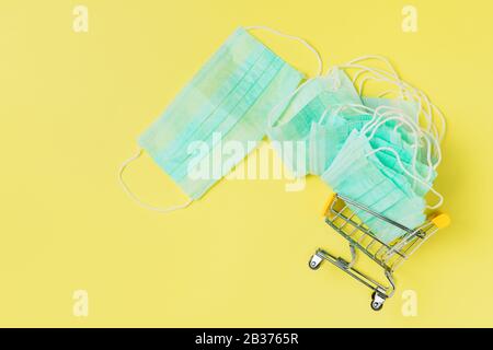 Maschera medica in un carrello, carrello su sfondo giallo, protezione personale e concetto di shopping Foto Stock