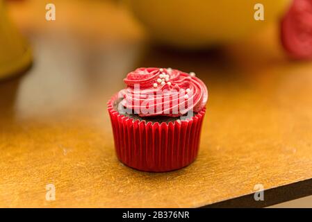 Vista dall'alto di deliziosi cupcake al cioccolato con glassa di crema rossa e spruzzette. Cupcake con la colorata glassa di Chantilly. Cupcake al cioccolato su tavolo di legno. Foto Stock