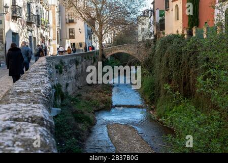 Rio Darro sulla sua strada attraverso Granada con un ponte e persone a piedi lungo Carrera del Darro strada Foto Stock