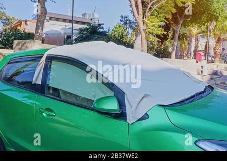 Parabrezza di auto con superficie protettiva in tessuto di tessuto protettivo crema solare su auto parcheggiata in strada calda giorno con raggi di sole. Metodo per proteggere riscaldato da raggi solari all'interno dell'auto Foto Stock