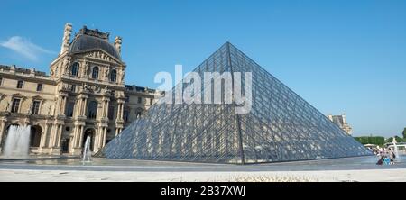 Vista panoramica della Cour Napoleon del museo del Louvre con la famosa piramide di vetro modernista, uno dei principali ingressi al museo Foto Stock