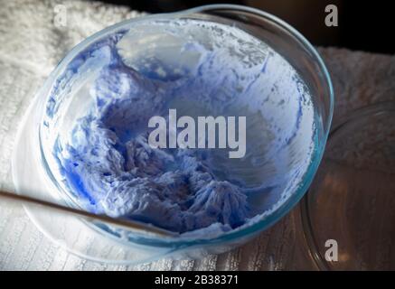 Prodotto colorante per capelli. Candeggina per capelli. Ciotola con perossido e pennello, primo piano su uno sfondo viola. Foto Stock