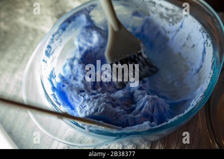 Prodotto colorante per capelli. Candeggina per capelli. Ciotola con perossido e pennello, primo piano su uno sfondo viola. Foto Stock